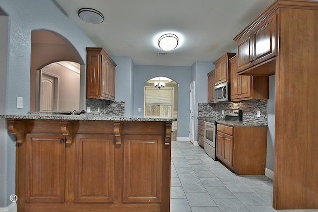 kitchen featuring light stone counters, kitchen peninsula, appliances with stainless steel finishes, and tasteful backsplash