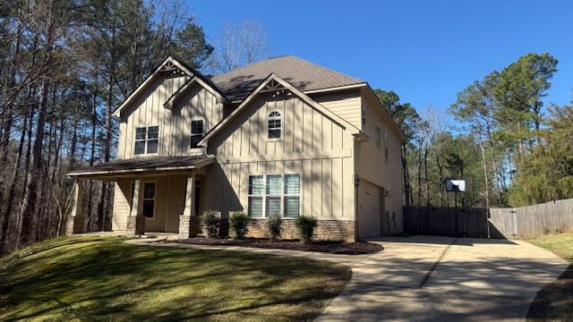 view of front of property with concrete driveway, board and batten siding, fence, a garage, and a front lawn