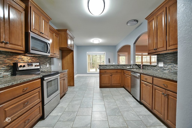 kitchen with decorative backsplash, appliances with stainless steel finishes, sink, and dark stone countertops