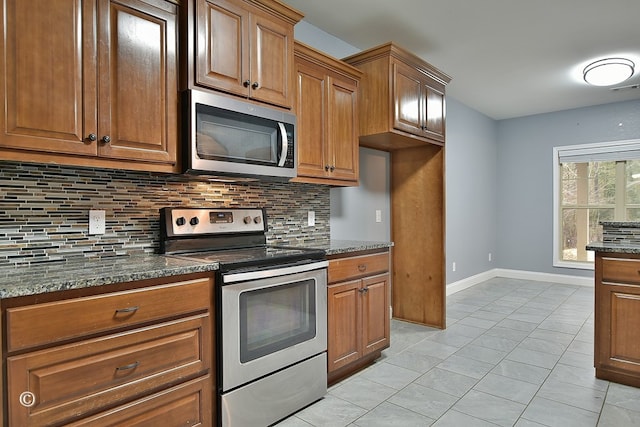 kitchen with dark stone countertops, decorative backsplash, light tile patterned flooring, and stainless steel appliances