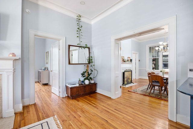 corridor with crown molding, baseboards, light wood-type flooring, and a notable chandelier
