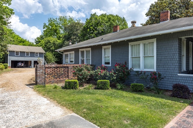 view of front of house featuring roof with shingles, dirt driveway, a chimney, and a front yard