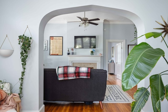 living area with crown molding, arched walkways, ceiling fan, and wood finished floors