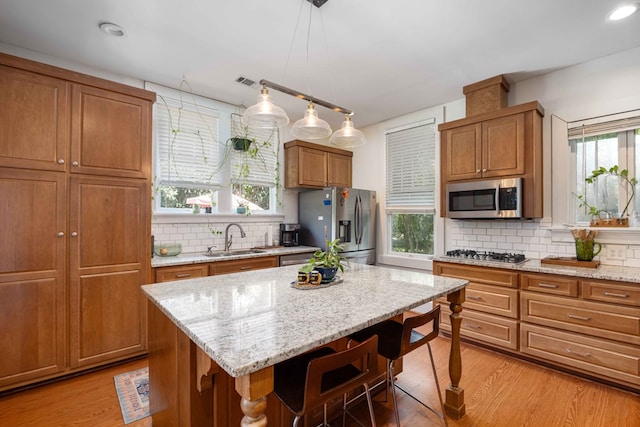 kitchen with brown cabinets, appliances with stainless steel finishes, a sink, light wood-style floors, and a breakfast bar area