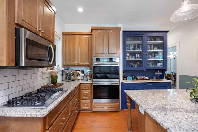 kitchen featuring brown cabinetry, appliances with stainless steel finishes, backsplash, and glass insert cabinets