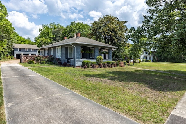 view of front of home with a porch, driveway, a chimney, and a front lawn