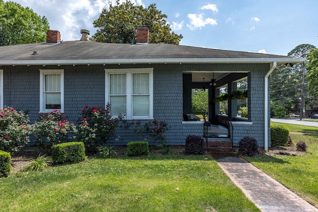 view of front of home with roof with shingles, covered porch, a chimney, and a front yard
