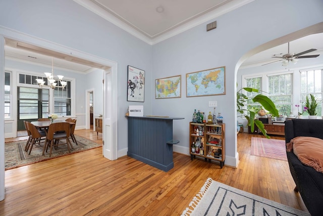 interior space featuring crown molding, arched walkways, light wood-style flooring, ceiling fan with notable chandelier, and baseboards