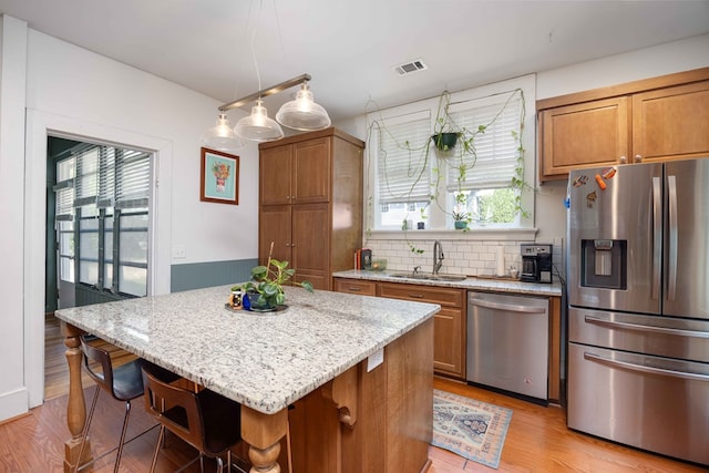 kitchen with brown cabinets, a sink, light stone counters, light wood finished floors, and stainless steel appliances