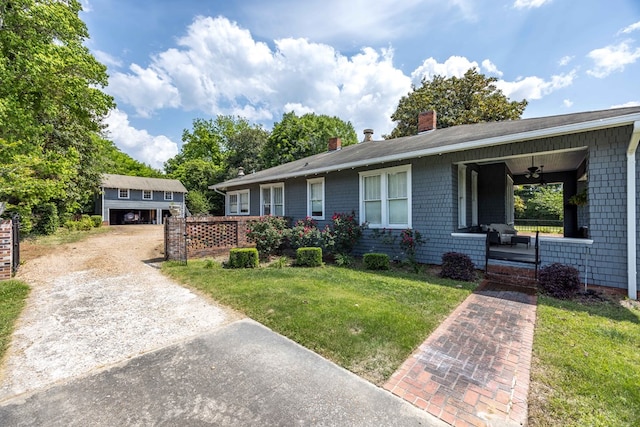 ranch-style home with a porch, a ceiling fan, a chimney, a front yard, and an outbuilding