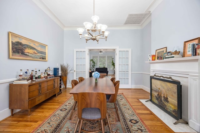 dining area with crown molding, visible vents, a fireplace with flush hearth, light wood-style flooring, and a notable chandelier