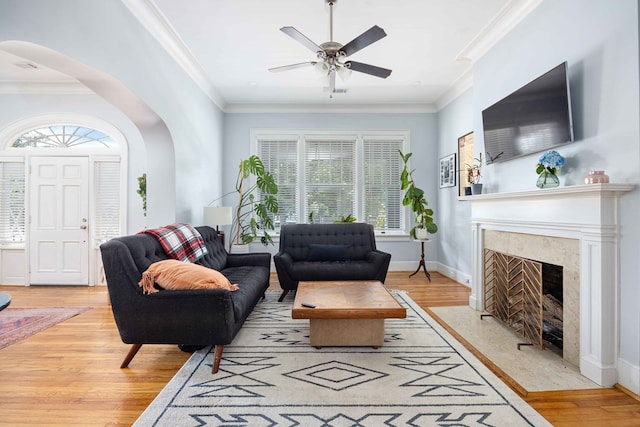 living room featuring light wood-style floors, arched walkways, plenty of natural light, and crown molding