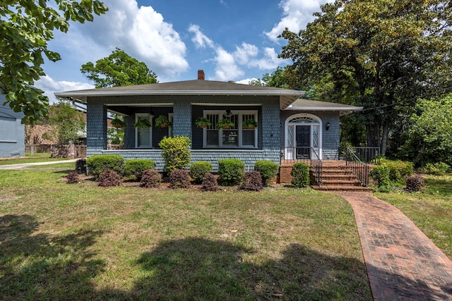 view of front of home with covered porch, a chimney, and a front yard