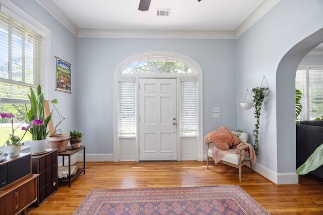 foyer with arched walkways, visible vents, ornamental molding, and light wood-type flooring
