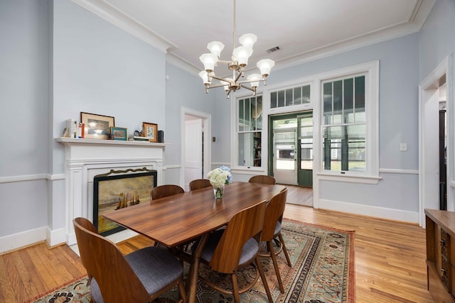 dining space featuring crown molding, light wood-style flooring, a notable chandelier, and a fireplace