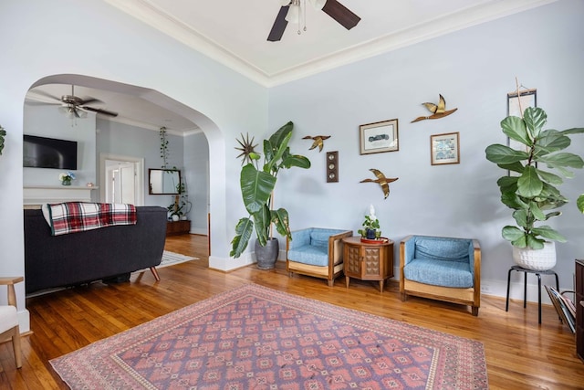 living area with crown molding, arched walkways, ceiling fan, and wood finished floors