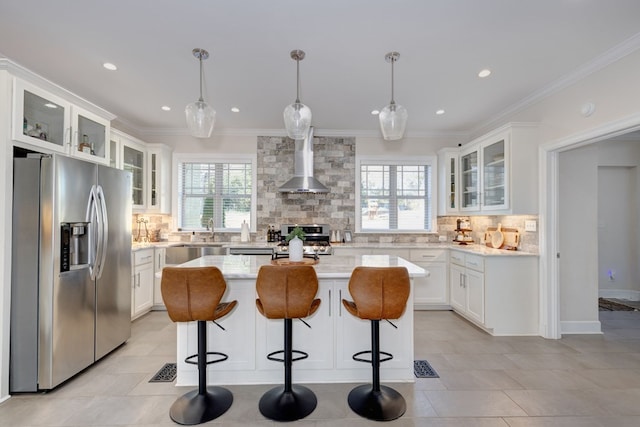 kitchen with white cabinets, stainless steel fridge, a kitchen island, and wall chimney range hood