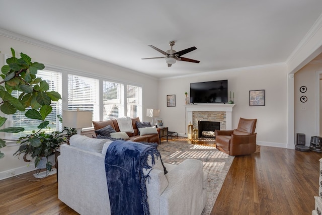 living room with dark hardwood / wood-style floors, ceiling fan, a stone fireplace, and crown molding