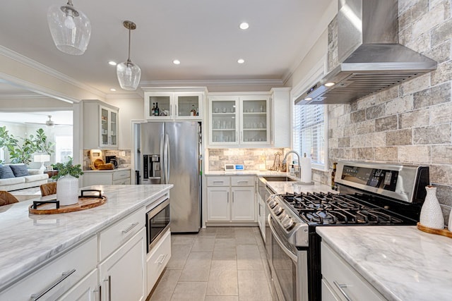 kitchen featuring white cabinets, wall chimney range hood, sink, appliances with stainless steel finishes, and decorative light fixtures