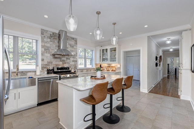 kitchen featuring wall chimney exhaust hood, stainless steel appliances, decorative light fixtures, white cabinets, and a kitchen island