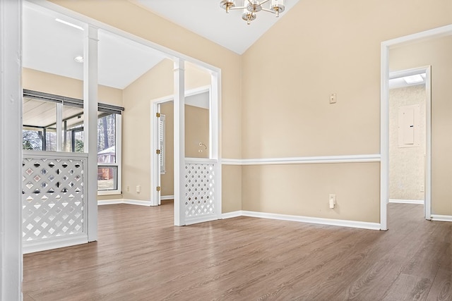 empty room with a notable chandelier, vaulted ceiling, wood finished floors, electric panel, and baseboards