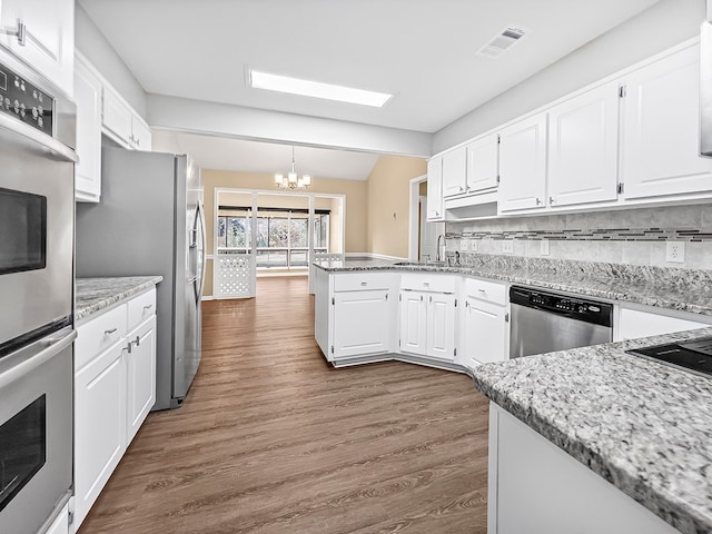 kitchen featuring appliances with stainless steel finishes, dark wood-type flooring, white cabinetry, a chandelier, and a peninsula