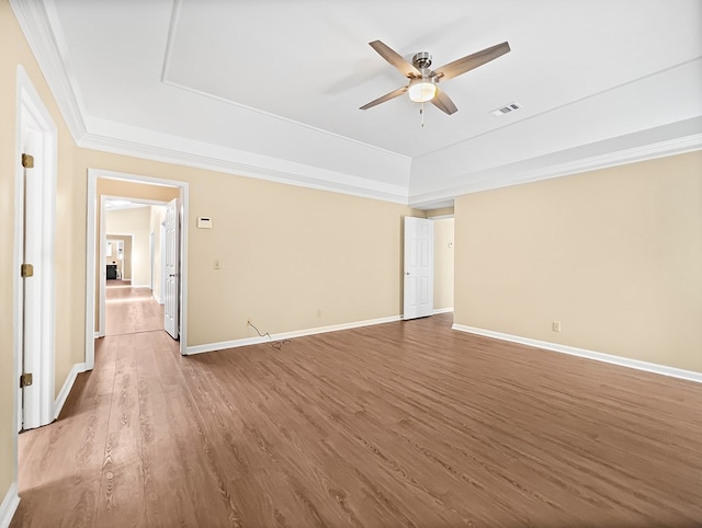 empty room with ceiling fan, visible vents, a raised ceiling, and wood finished floors