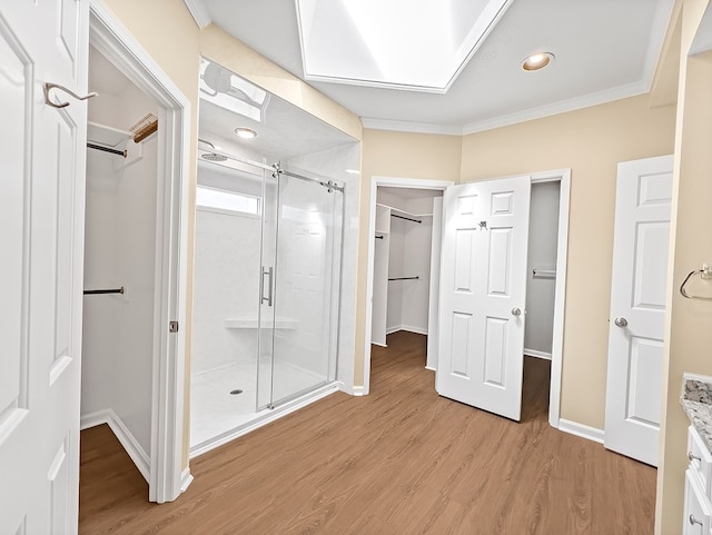 full bathroom featuring ornamental molding, wood finished floors, a walk in closet, vanity, and a shower stall