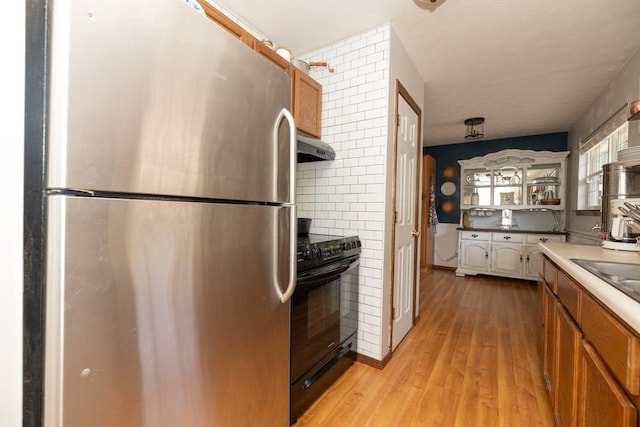 kitchen with exhaust hood, freestanding refrigerator, brown cabinets, light wood-type flooring, and black range with electric cooktop