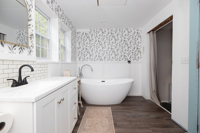 full bath featuring a wainscoted wall, wallpapered walls, a freestanding tub, wood finished floors, and vanity