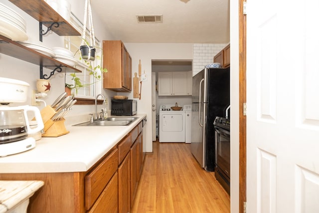 kitchen featuring a sink, washing machine and clothes dryer, light wood-style floors, black appliances, and visible vents