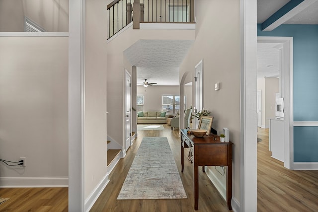 hall with a high ceiling, a textured ceiling, baseboards, and wood finished floors