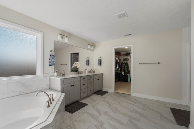 bathroom featuring visible vents, a garden tub, a walk in closet, a textured ceiling, and a sink