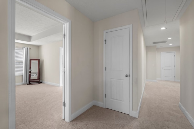 hall with carpet floors, attic access, visible vents, and baseboards