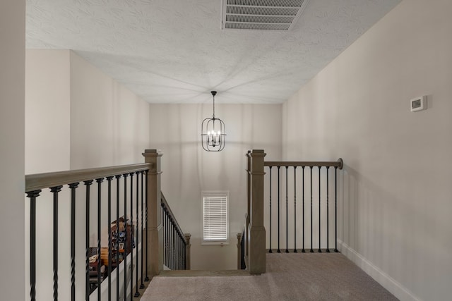 stairway with a textured ceiling, carpet floors, visible vents, baseboards, and an inviting chandelier