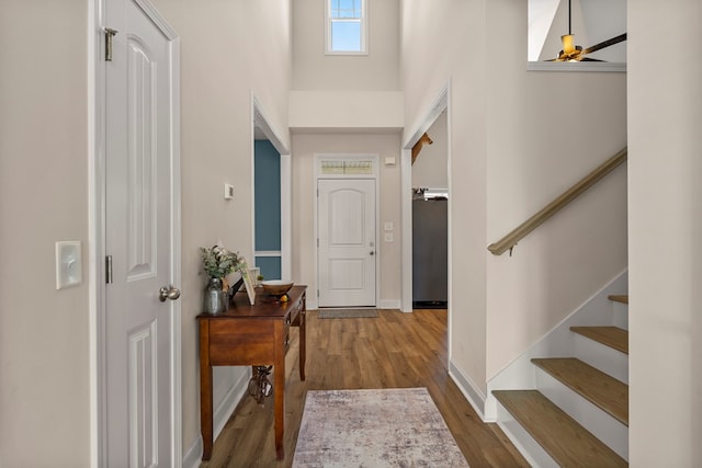 foyer entrance featuring a high ceiling, stairway, wood finished floors, and baseboards