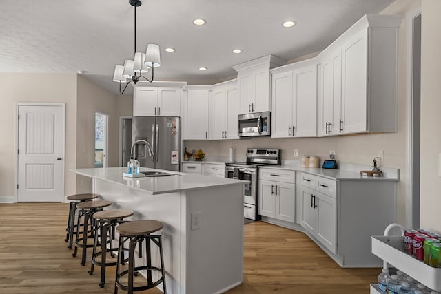 kitchen featuring light wood finished floors, light countertops, appliances with stainless steel finishes, a sink, and a kitchen bar