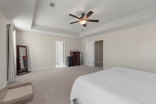 bedroom with ceiling fan, light colored carpet, visible vents, baseboards, and a tray ceiling