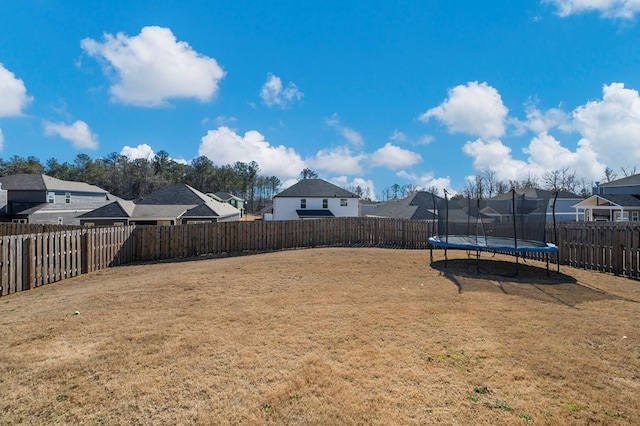 view of yard featuring a trampoline, a fenced backyard, and a residential view