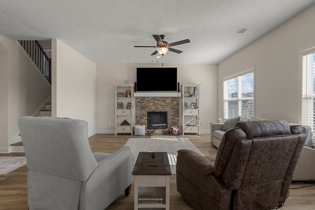 living room with a ceiling fan, visible vents, a stone fireplace, and wood finished floors