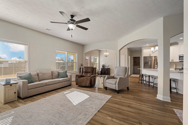 living area featuring ceiling fan with notable chandelier, arched walkways, a textured ceiling, and wood finished floors