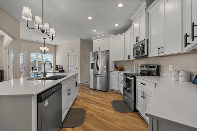 kitchen featuring arched walkways, appliances with stainless steel finishes, a sink, a kitchen island with sink, and a notable chandelier