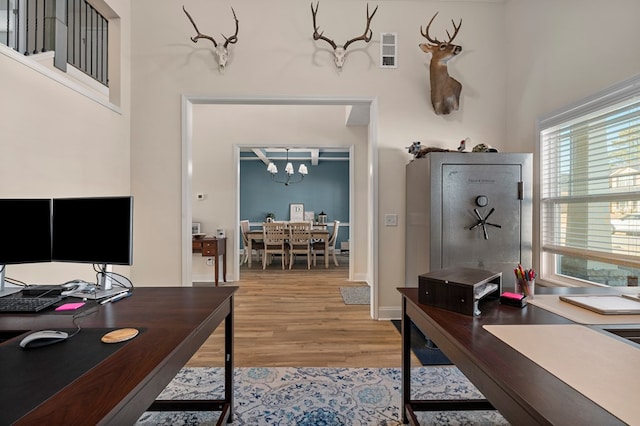 office area featuring light wood-type flooring, a towering ceiling, visible vents, and an inviting chandelier