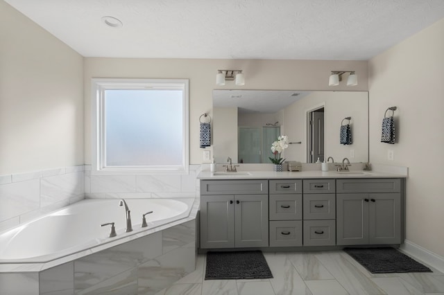 bathroom featuring a bath, a textured ceiling, double vanity, and a sink