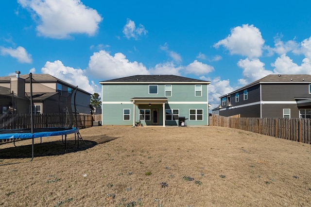 rear view of house featuring a trampoline, a fenced backyard, and a lawn