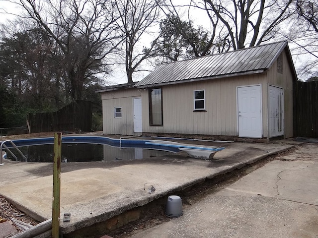 outdoor pool with a patio, fence, a diving board, and an outdoor structure