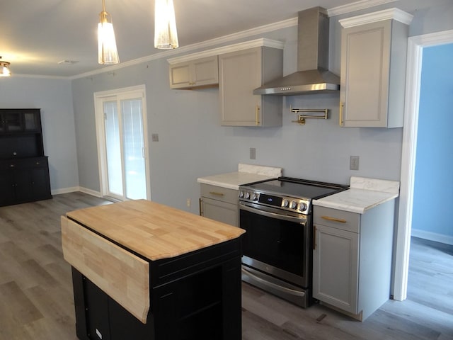 kitchen featuring light wood finished floors, wall chimney exhaust hood, crown molding, and stainless steel range with electric cooktop