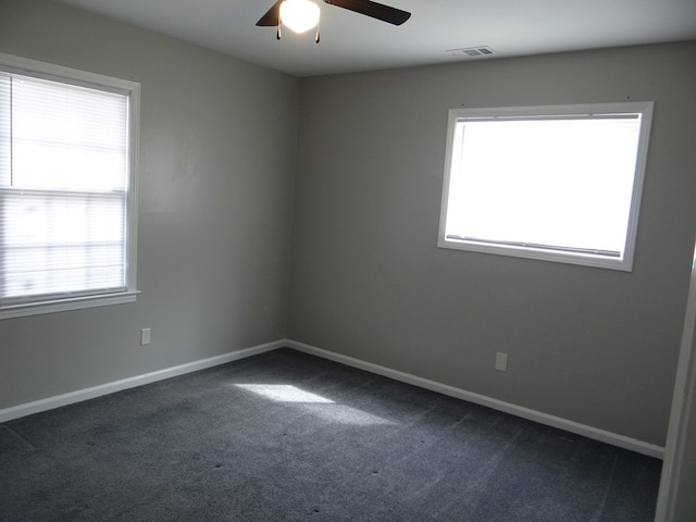 empty room featuring dark colored carpet, visible vents, baseboards, and a ceiling fan