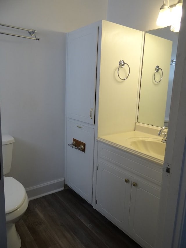 half bath featuring vanity, toilet, wood finished floors, and baseboards