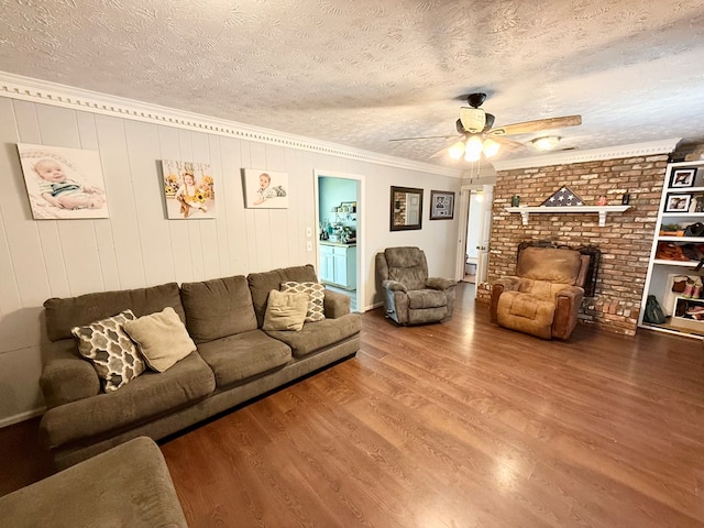 living area featuring a textured ceiling, ceiling fan, a brick fireplace, crown molding, and wood finished floors